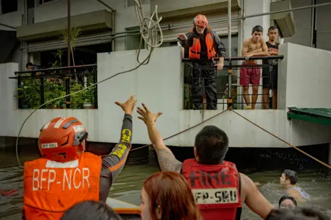 Ezra Acayan/Getty Images Rescuers reach for a rope as they ride a boat to reach residents trapped by flooding caused by Typhoon Gaemi and monsoon rains on July 24, 2024 in Quezon city, Metro Manila, Philippines.