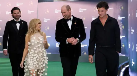 Reuters Kylie Minogue and Shawn Mendes walk along a green carpet with Prince William.