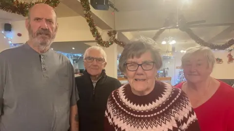 James Jones and his wife Christine flank his mum Evelyn Williams and stepdad Harry, with Christmas decorations in a hall behind them.